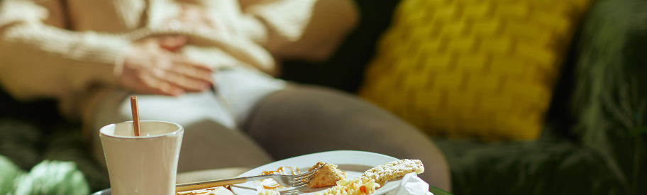 Persoon hand op buik in de bank voor de persoon bord met half opgegeten eten